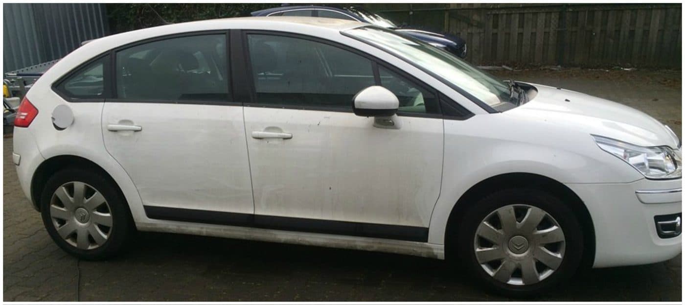 Witte Citroën C4 met een vuile, dofgrijze zijkant en aanslag langs de dorpels, geparkeerd op een oprit.