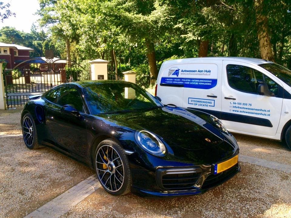 Een pas gewassen zwarte Porsche op een oprit, met daarachter de bestelbus van Autowassen aan huis met de bedrijfsnaam op de zijkant.